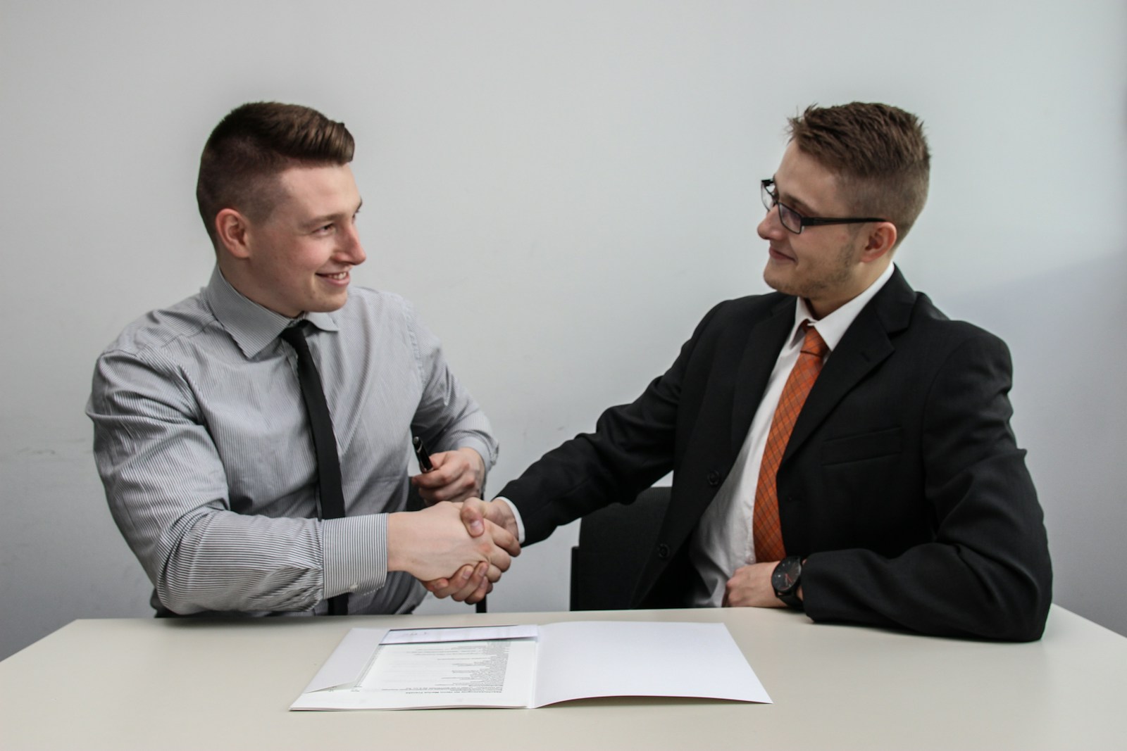 two men facing each other while shake hands and smiling becaue they have business insurance